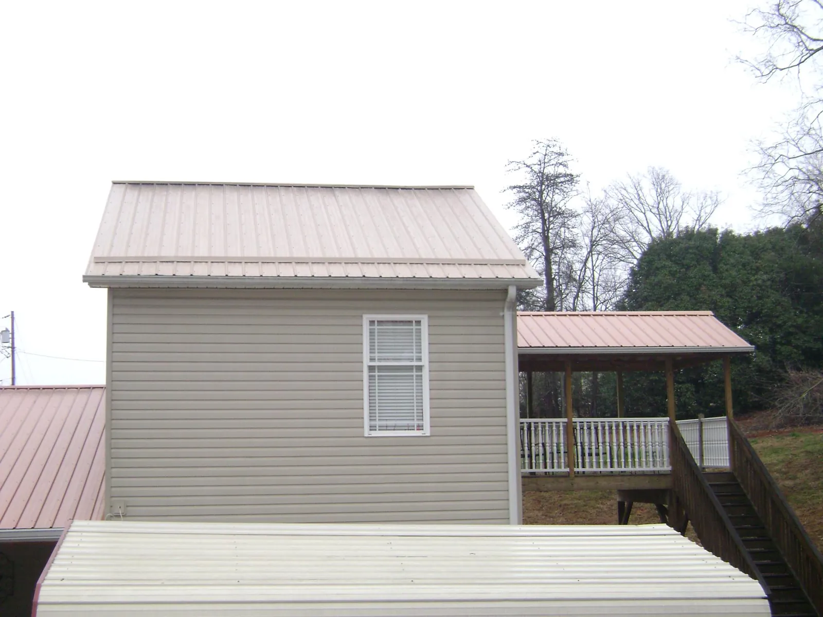 Tan metal roofs on a two story addition and attached porch, from a Roof Replacement job in Lakeside